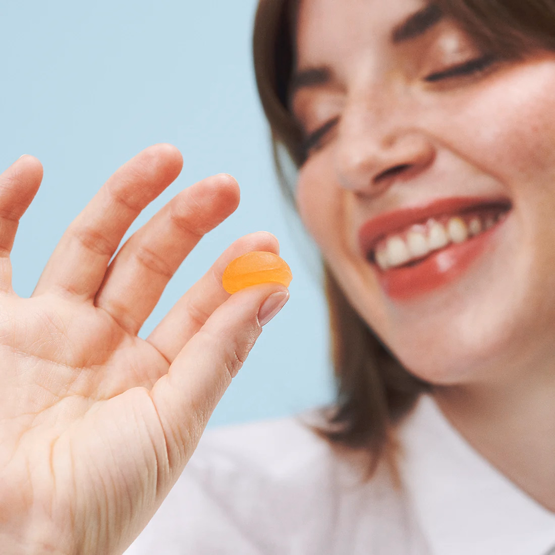 A woman holding an orange gummy in front of a blue background